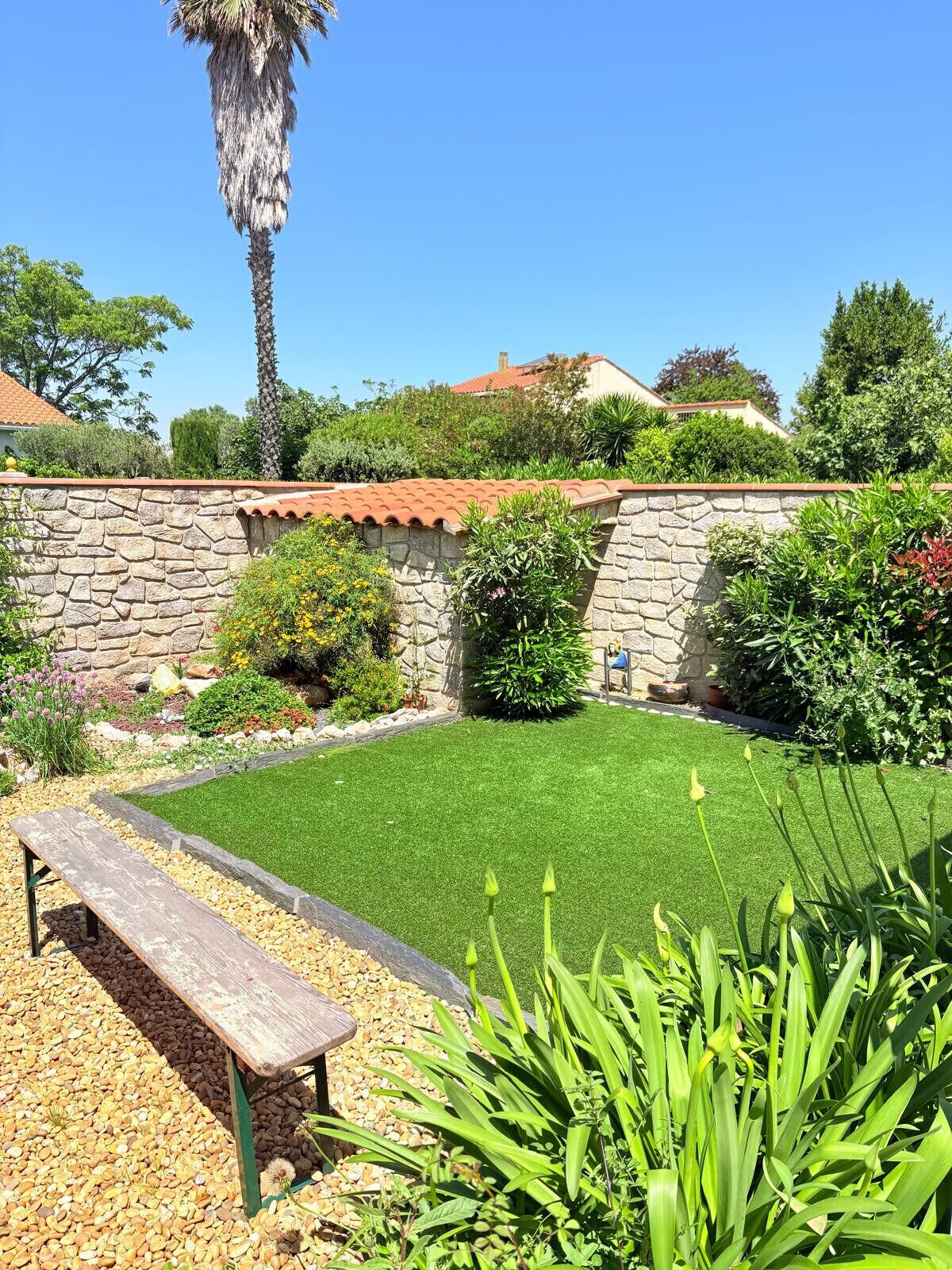 Un jardin avec un mur de pierre, un banc et différentes plantes.