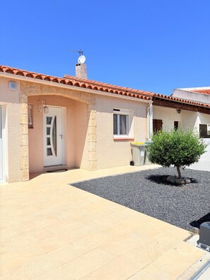Une maison avec un toit en tuiles, un petit jardin avec un arbre et une allée gravillonnée.