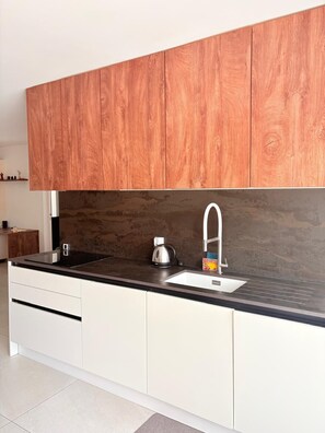Une cuisine moderne avec des meubles en bois, un plan de travail noir, un évier en acier inoxydable et une bouilloire.