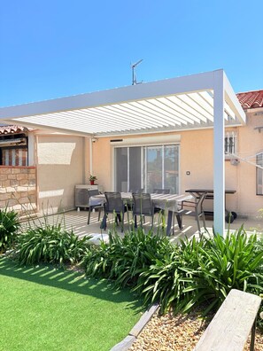 Une terrasse couverte avec une table et des chaises, une porte-fenêtre coulissante et un mur en pierre.