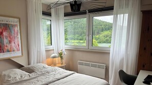 Ein Schlafzimmer mit Bett, Schreibtisch, Stuhl, Heizkörper und Fenster mit Blick auf einen Wald und ein See.
