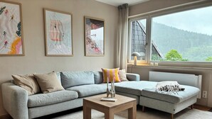 Una sala de estar moderna con un sofá gris, una mesita y una ventana con vistas a un bosque.