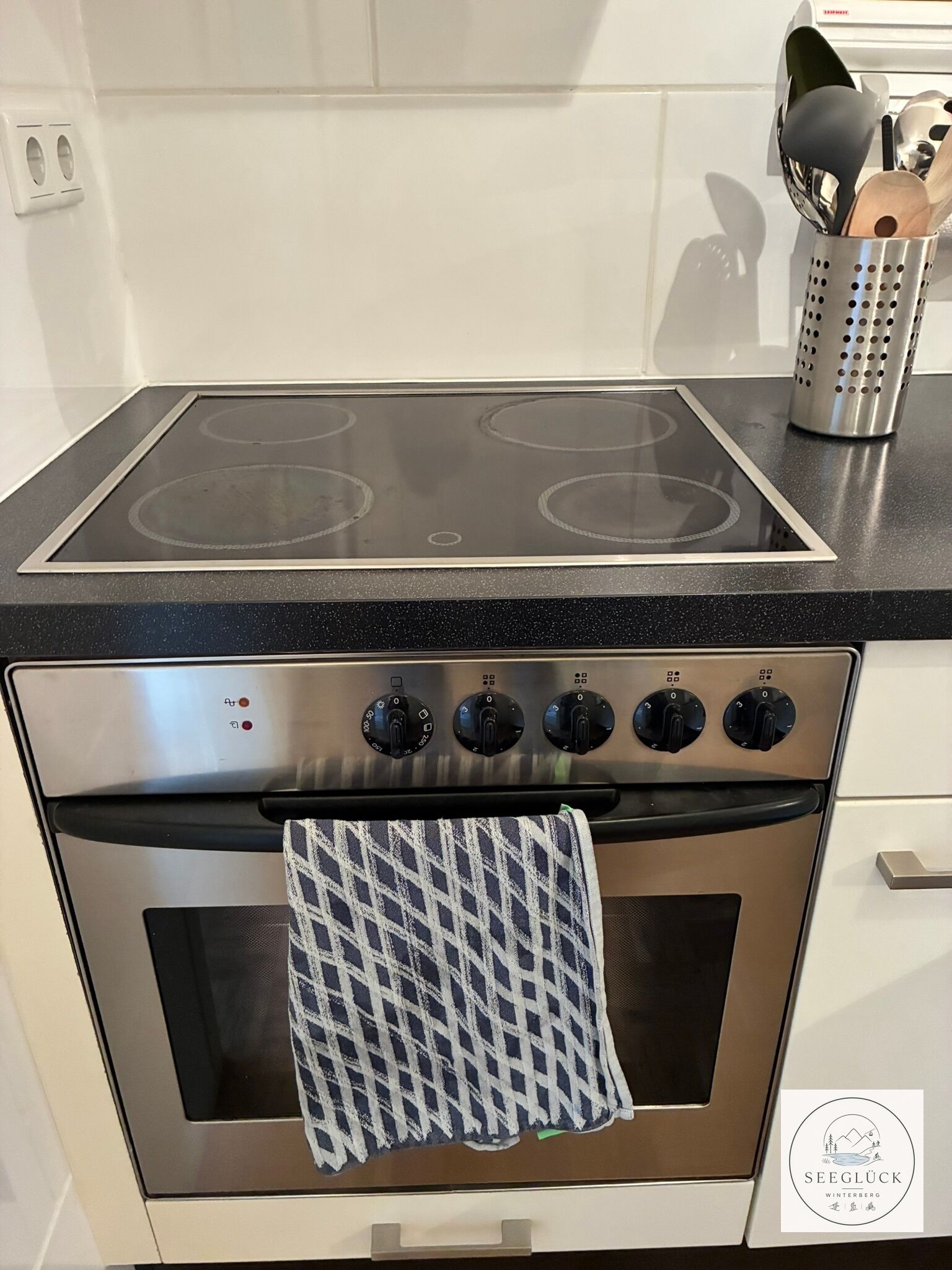 A kitchen with a stainless steel stove, a black countertop, and a stainless steel utensil holder.