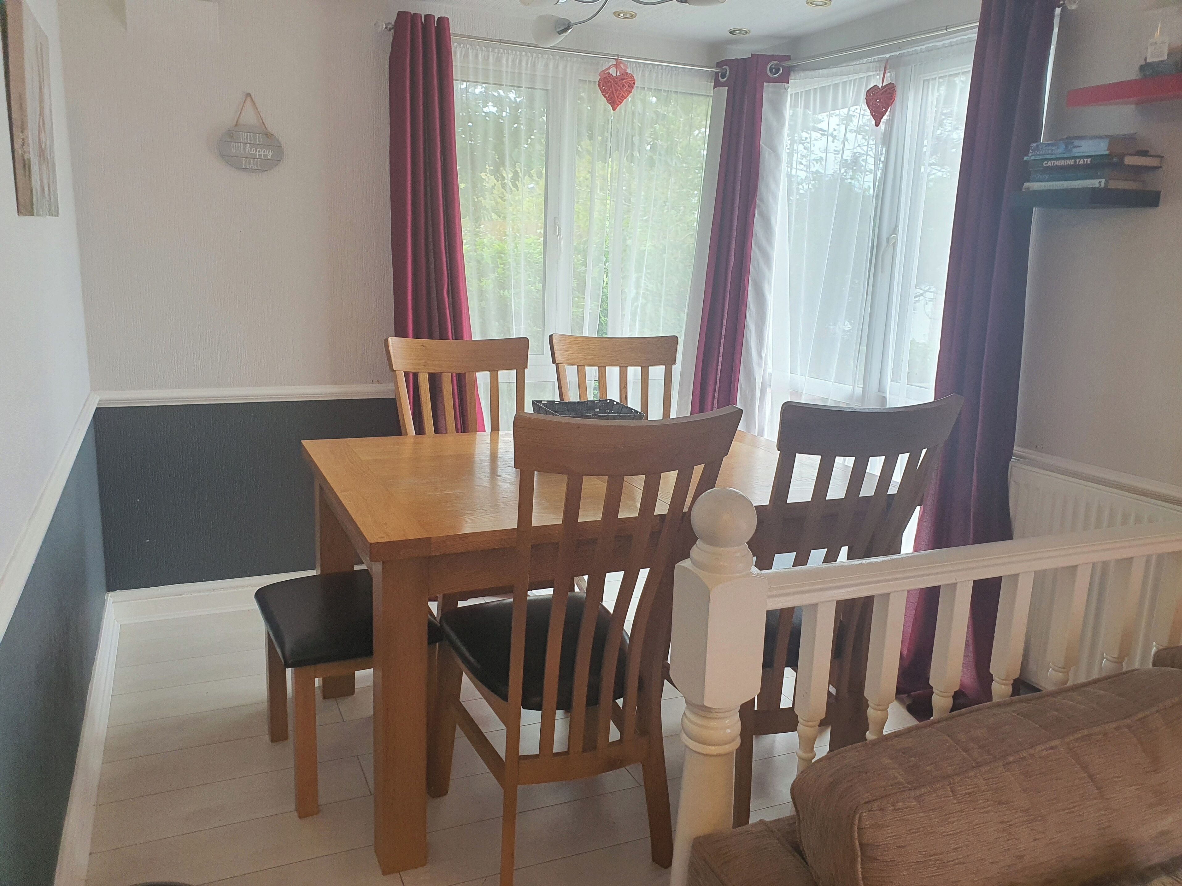 Een eethoek met een houten tafel en stoelen, een bankje, en uitzicht op de omgeving door een raam met gordijnen.