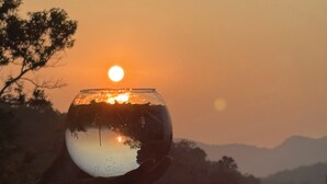 A glass bowl with a sunset reflection, held against a backdrop of a mountainous landscape. - OBEROI RESIDENCY  (Pachmarhi)