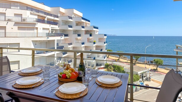 A table set for dining with a view of the sea and buildings in the background. - Maricel apartment with pool and sea views (L'Escala)