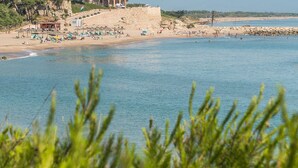 A beach with clear blue water, a sandy shore, and a stone wall in the background. - Maricel apartment with pool and sea views (L'Escala)