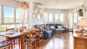 A spacious living area with a dining table, chairs, a sofa, and a lamp. - Maricel apartment with pool and sea views (L'Escala)