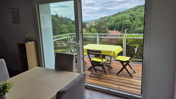 A balcony with a table and chairs, a view of a green landscape, and a door leading to the balcony. - The edge of the vineyard - the balcony (Andlau)