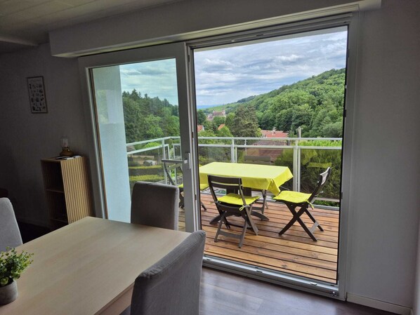Ein Balkon mit Tisch und Stühlen, Blick auf eine grüne Landschaft und eine Tür, die auf den Balkon führt.