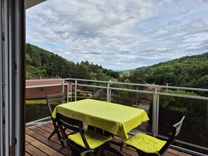 A balcony with a table and chairs, overlooking a valley with houses and greenery. - At the Edge of the Vineyard—The Balcony (Andlau)