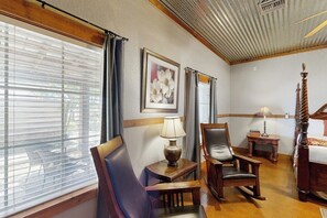 Ein Hotelzimmer mit großem Fenster, einem hölzernen Bett, einem Sessel, einem Nachttisch und einer Lampe.