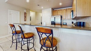 A kitchen with a central island, bar stools, wooden cabinets, and a refrigerator. - Dog-friendly & spacious condo with lake views, large balcony, & Pool (Horseshoe Bay)