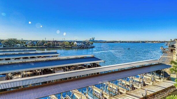 A waterfront property with multiple dock areas, a boat, and a clear view of the water. - Dog-friendly & spacious condo with lake views, large balcony, & Pool (Horseshoe Bay)