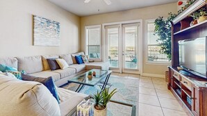 A living room with a sofa, coffee table, TV, and a ceiling fan. - Dog-friendly & spacious condo with lake views, large balcony, & Pool (Horseshoe Bay)