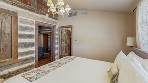 Una camera da letto con un letto, un lampadario, pareti in legno e una porta che dà su un'altra stanza.