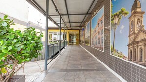 A covered walkway with tiled flooring, a metal railing, and a mural of a building on the wall. - TRI HOTEL SMART SANTA MARIA (Santa Maria)
