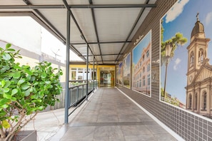 A covered walkway with tiled flooring, a metal railing, and a mural of a building on the wall.