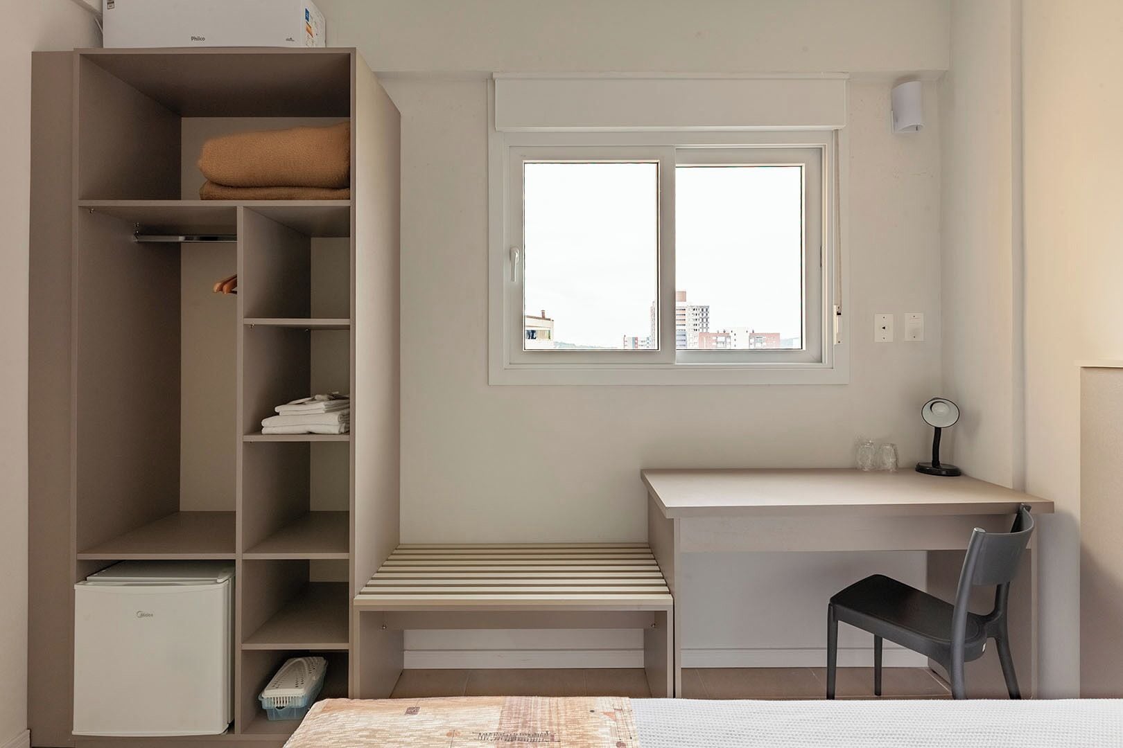 A bedroom with a bed, a desk, a chair, a wardrobe, and a window.