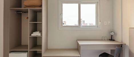 A bedroom with a bed, a desk, a chair, a wardrobe, and a window.