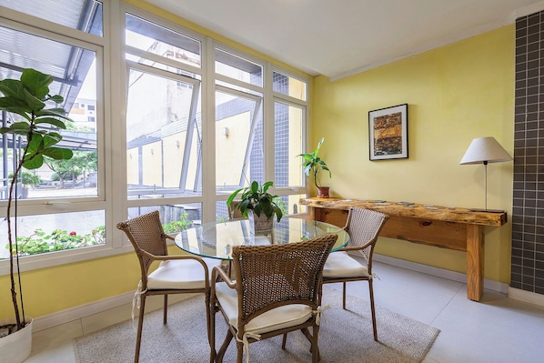 A dining area with a glass table, wicker chairs, a wooden bench, a potted plant, and a lamp.