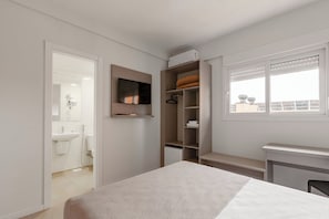A bedroom with a bed, a TV mounted on the wall, a wardrobe, and a window with blinds.