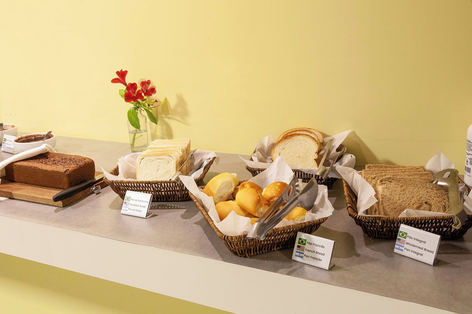 A buffet with various breads and a cake, labeled with types like 'Pão Integral' and 'French Bread'.