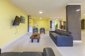 A modern lobby with a flat-screen TV, two armchairs, a sofa, a coffee table, and a tiled accent wall. - TRI HOTEL SMART SANTA MARIA (Santa Maria)