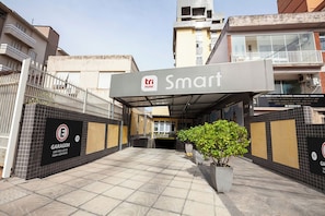 A hotel entrance with a sign reading 'Tri Hotel Smart,' a gated garage area, and tiled flooring.