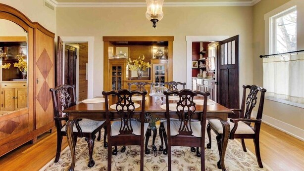 Una sala da pranzo con tavolo e sedie in legno, un lampadario e vista sulla cucina.