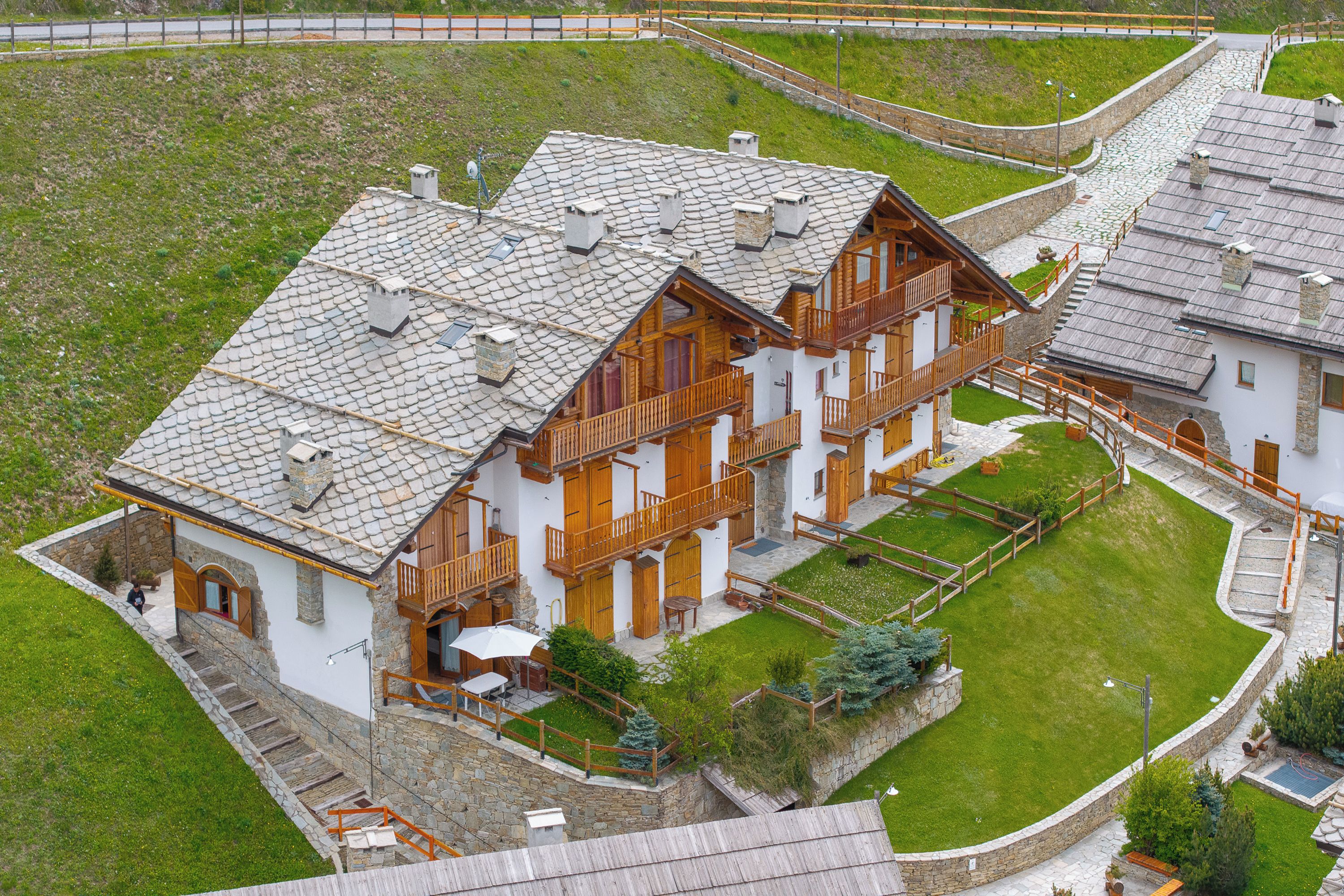 A multi-story building with a stone facade, wooden balconies, and a well-maintained lawn.