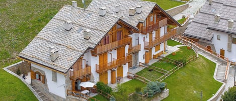 A multi-story building with a stone facade, wooden balconies, and a well-maintained lawn.