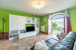 A living room with a TV, white entertainment unit, green walls, a leather sofa, and a view through a glass door. - La Casa Di Olaf (Bardonecchia)