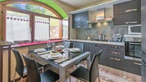 A modern kitchen with a dining area, featuring a stone wall, dark cabinetry, and a built-in oven. - La Casa Di Olaf With Garden (Bardonecchia)