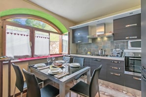 A modern kitchen with a dining area, featuring a stone wall, dark cabinetry, and a built-in oven. - La Casa Di Olaf (Bardonecchia)