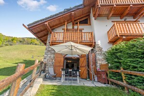 A wooden chalet with a stone facade, a balcony, and a patio area with outdoor seating. - La Casa Di Olaf (Bardonecchia)