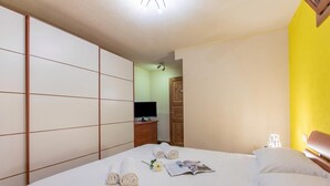 A neatly made bed with rolled towels and a magazine, a television on a wooden dresser, and a wooden wardrobe. - La Casa Di Olaf With Garden (Bardonecchia)