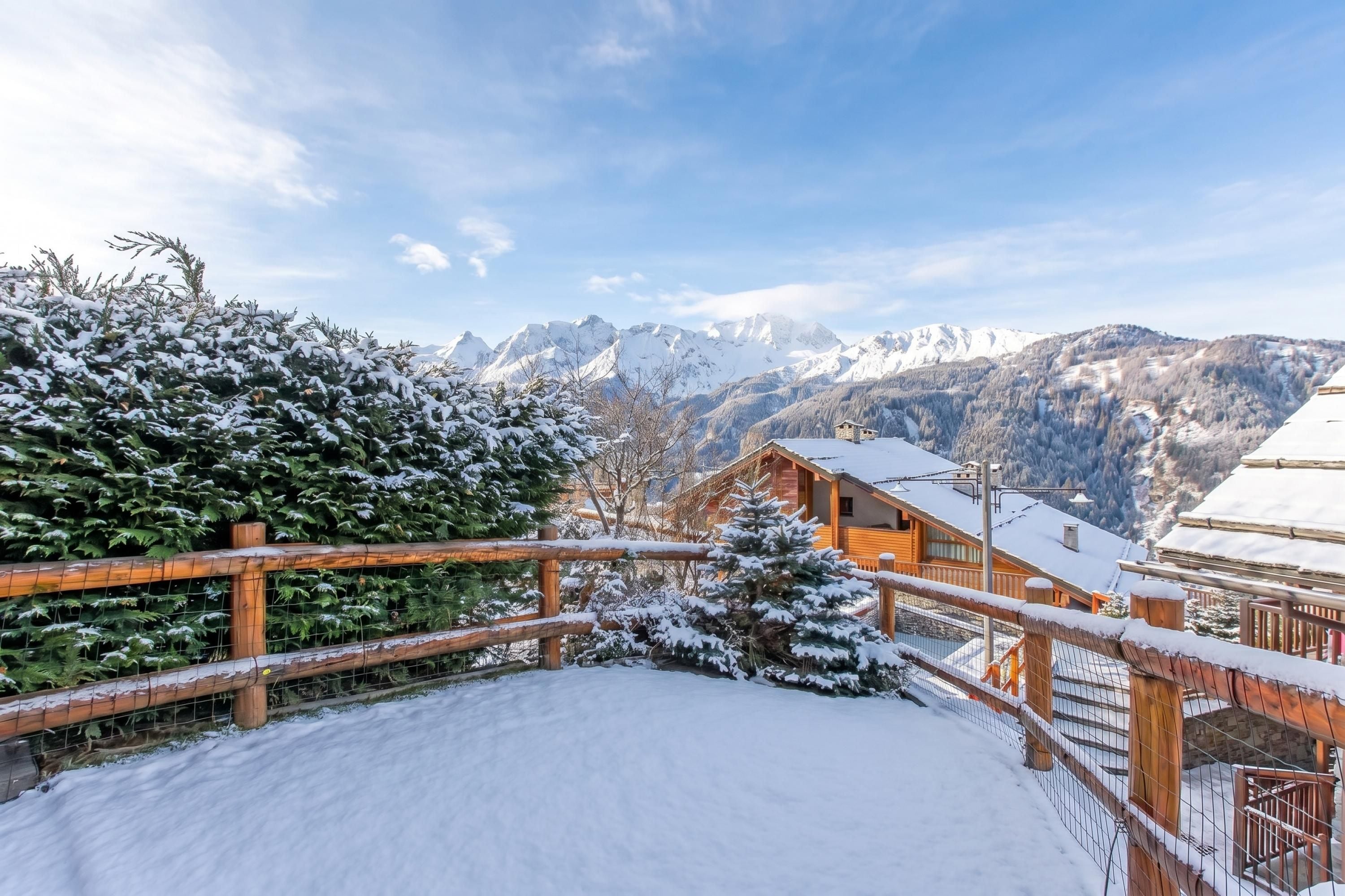 Ein mit Schnee bedeckter Holzboden mit Blick auf verschneite Berggipfel im Hintergrund.