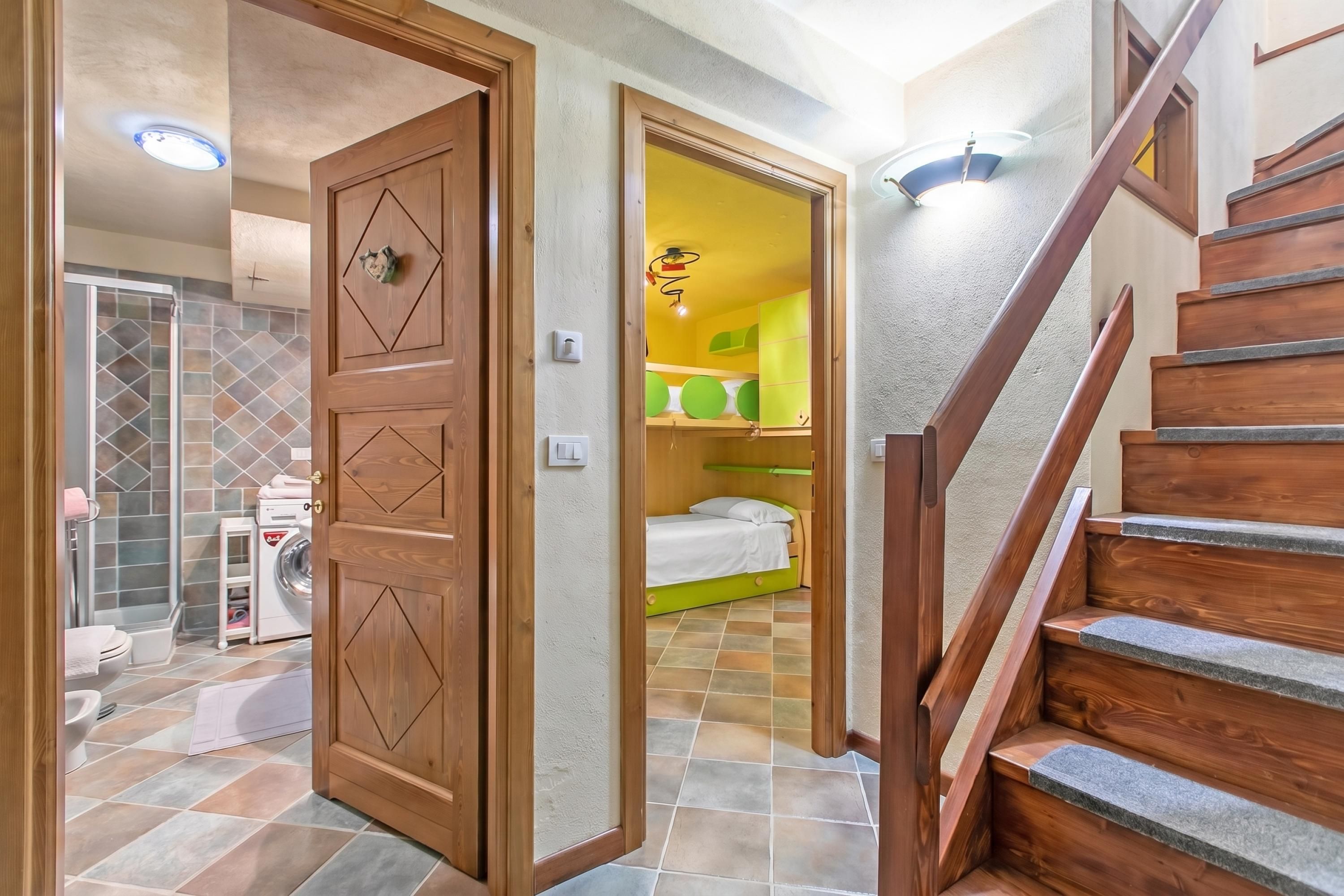 Un pasillo con una puerta de madera que da a un baño, una escalera y una habitación con cama y paredes verdes.