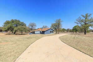 A house with a paved driveway, surrounded by trees and open grassy areas. - Secluded, Dog-Friendly Getaway w/ Beautiful Views, a Large Yard, & Free WiFi (Fredericksburg)