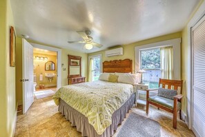 Ein Schlafzimmer mit Bett, Nachttisch, Sessel, Deckenventilator, Fenster und Klimaanlage.
