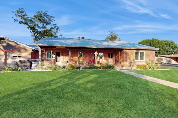 A single-story brick house with a covered porch, a front yard, and a garage. - Charming, dog-friendly home with patio, grill, & parking - close to town (Fredericksburg)