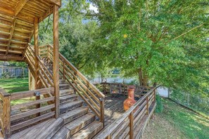 Eine Holzterrasse mit einer Treppe zu einem ĂŒberdachten Bereich, umgeben von BĂ€umen und einem eingezĂ€unten Garten.