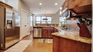 A modern kitchen with stainless steel appliances, wooden cabinets, and a granite countertop.
