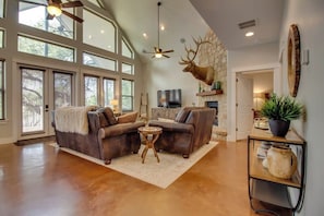 A spacious living room with a large window, a fireplace, and a mounted deer head.