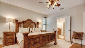 A bedroom with a wooden bed, bedside lamps, a ceiling fan, and a door leading to another room.