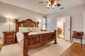 A bedroom with a wooden bed, bedside lamps, a ceiling fan, and a door leading to another room.