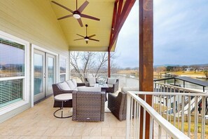 A covered outdoor area with a ceiling fan, wicker furniture, and a view of the surrounding landscape. - Charming lakefront home with lake views, dock & entertainment (Burnet)