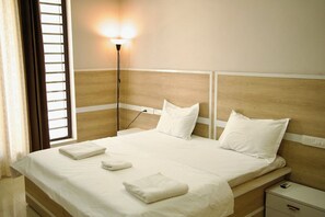 Et hotelværelse med seng, natbord, lampe og et vindue med gardiner.
