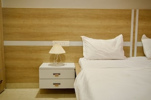 Une chambre à coucher bien rangée, avec une tête de lit en bois, une table de chevet avec une lampe et un lit recouvert de linge de lit blanc.